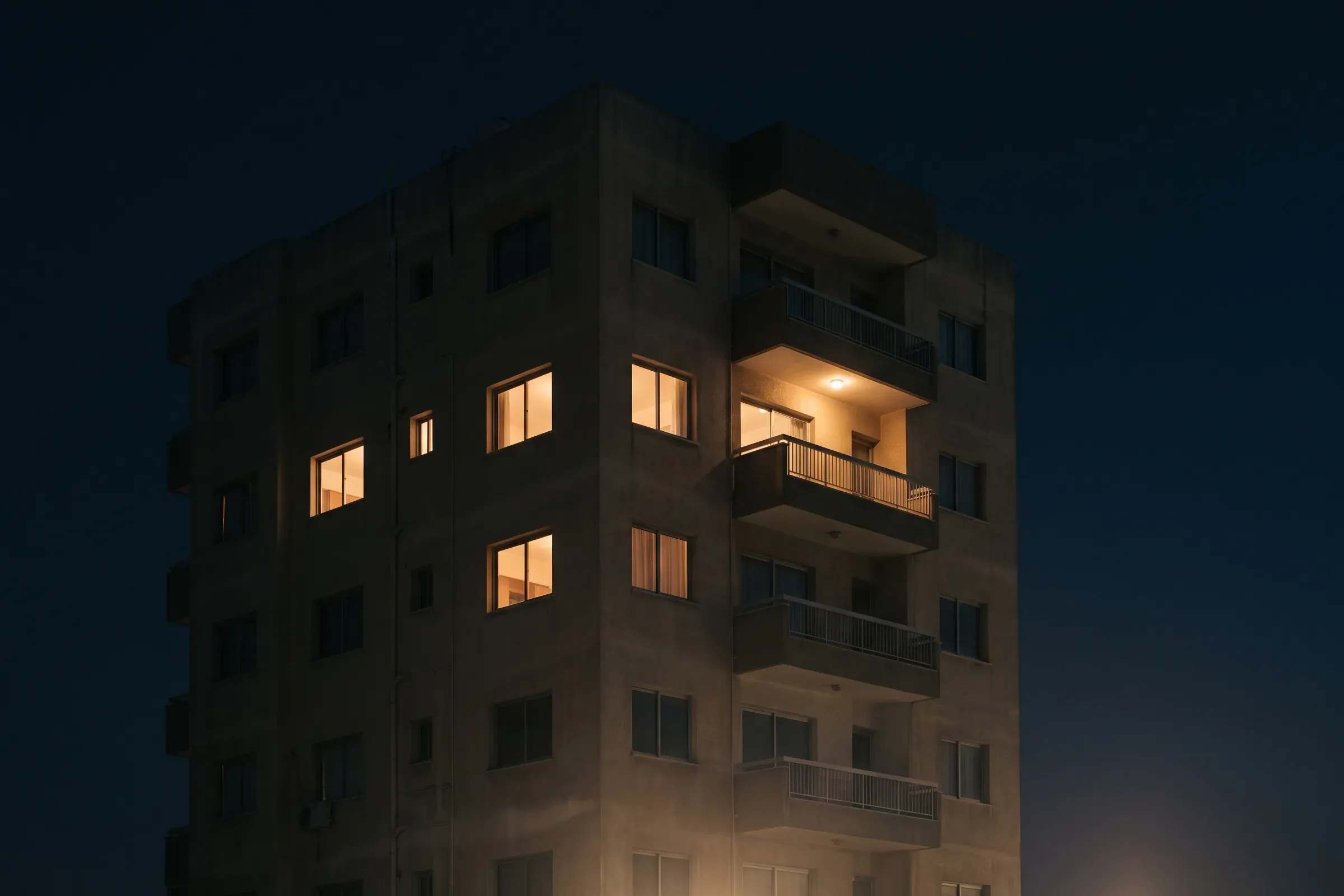 An apartment building at night, a few windows lit